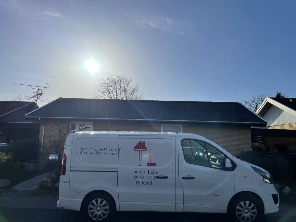 Tømrerbil parkeret foran et hus i solskin